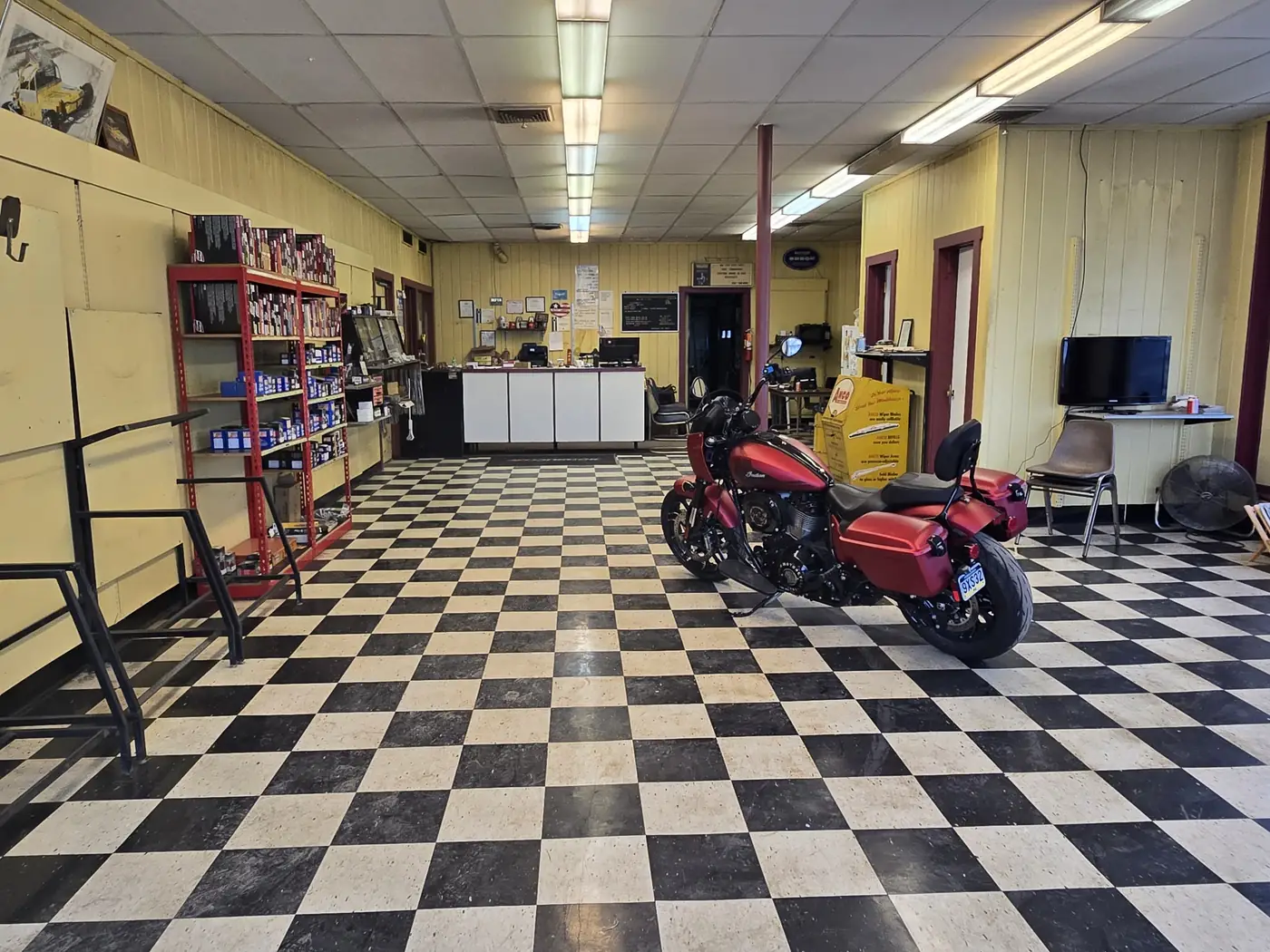 The front counter at Cutts and Bruises, with shelves of parts and a motorcycle parked on the checkerboard floor